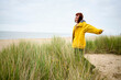 © Connect Images - Woman in a yellow raincoat enjoying the calm at a beach with tall grass, Belgium