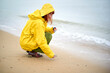 © Connect Images - Person in a yellow raincoat crouching on a sandy beach collecting shells, Belgium