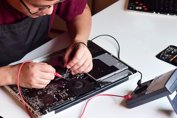 computer technician wearing glasses a laptop motherboard repairman is using an ic meter to find faul