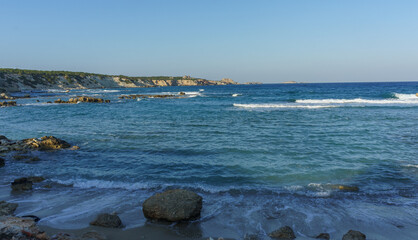 Wall Mural - Tranquil coastal view at sunset, waves gently lapping against rocky shore near serene cliffs.