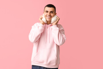 Poster - Handsome young man in warm fluffy earmuffs on pink background