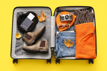 Wall Mural - Open packed suitcase with clothes, accessories, shoes and autumn leaves on yellow background