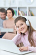 © aletia2011 - Cheerful little girl using a laptop at home with her parents in the background.