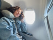 © Юлия Завалишина - Rest on plane. Young woman napping sitting by porthole in business jet using neck pillow for travel. Passenger girl flying in plane. Girl sleeping in airplane going on trip vacation. Traveling girl