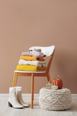 Wall Mural - Stack of stylish clothes, boots and autumn decorations on chair near beige wall in room