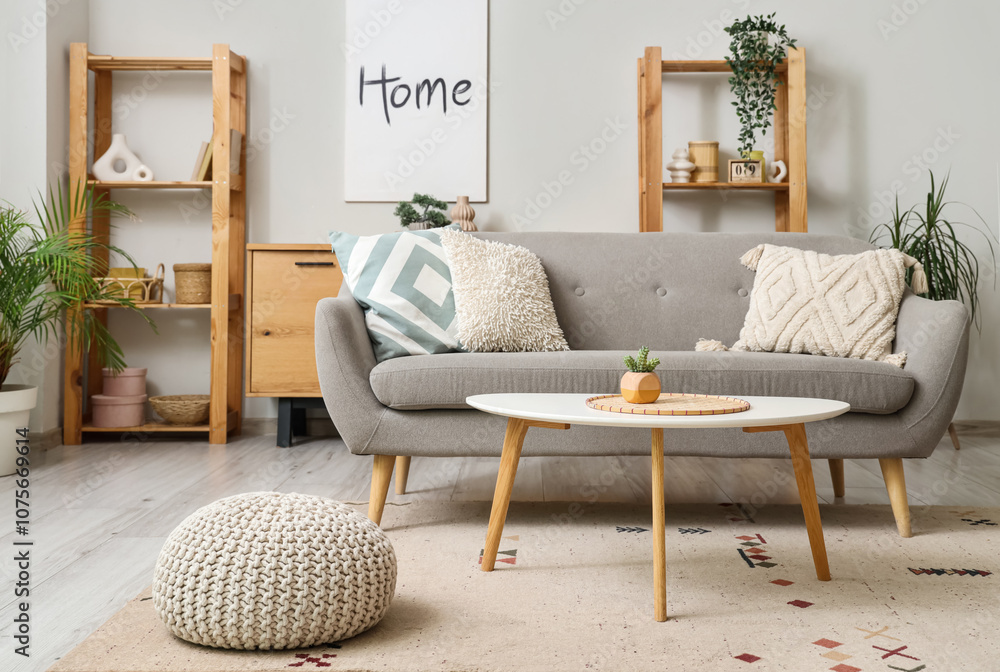 Interior of light living room with grey sofa, table and shelf units