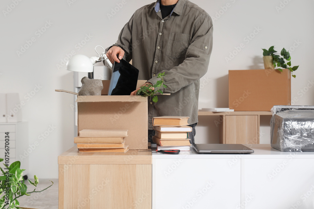 Male worker packing things at desk in office on moving day