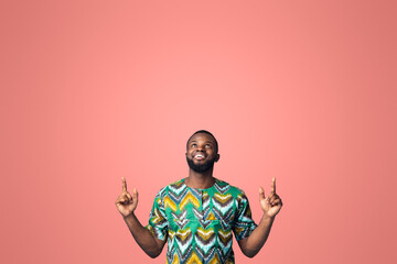 Wall Mural - Happy black guy in african costume pointing up at free space, showing advertisement on blue studio background. Positive african american man looking up, directing at empty space for text