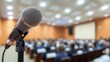 © Saowanee - A close-up of a microphone on a high stand positioned in the lower left corner, with a blurred background showing an attentive crowd, creating a focused event atmosphere.