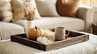 © Poomtan - A coffee table in a living room with a rustic tray holding a candle, a small pumpkin, and a mug of hot chocolate, with a sofa in warm, neutral tones in the background