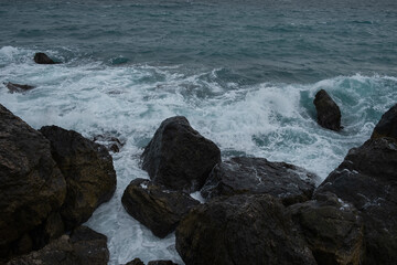 Turquoise sea stone beach, breaking waves on a cloudy spring day. Beautiful sea background. The concept of summer, vacation, travel. The purest clear sea water, large stones on the beach close-up