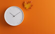 © Curioso.Photography - Minimalist clock on an orange background with a single autumn leaf, evoking a seasonal theme.