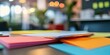 © Kamal - The blurred backdrop showcases blank sheets of colorful paper along with a bokeh effect, creating a visually appealing flat lay of an office workspace.
