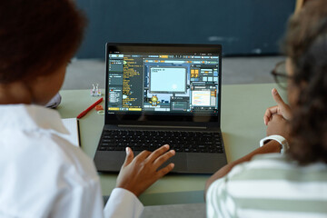 Over shoulder view of two kids using laptop in school classroom together with playful IT programming lesson on screen copy space