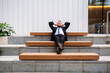© Westend61 - Smiling businessman relaxing on steps in front of wall