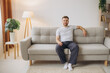 © anatoliycherkas - Joyful young bearded man in pajamas sitting on a sofa in living room at home with copy space