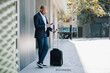 © Westend61 - Businessman standing with suitcase and using mobile phone on sunny day