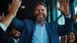 © angel_nt - joyful man, dressed in a suit, raises his arms in celebration surrounded by smiling colleagues in a well-lit office setting. Its an uplifting moment filled with camaraderie and positivity