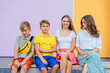 © Iryna - Group of four children friends sitting on bench against colorful wall