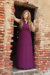 Elegant woman in purple dress holding champagne in rustic brick archway.Wine Day.