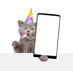 Aufkleber - Winking kitten with tongue out wearing party cap shows big smartphone with blank screen above empty white banner. Empty space for text. isolated on white background