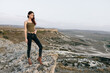 © VICHIZH - Woman in jeans and green tank top standing on cliff overlooking lush valley landscape