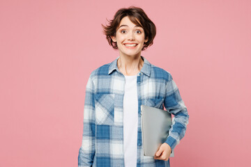 Young surprised happy fun IT woman she wears blue shirt white t-shirt casual clothes hold closed laptop pc computer isolated on plain pastel light pink background studio portrait. Lifestyle concept.