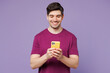 © ViDi Studio - Young happy Caucasian man he wear violet t-shirt casual clothes hold in hand use mobile cell phone texting message isolated on plain pastel light purple background studio portrait. Lifestyle concept.