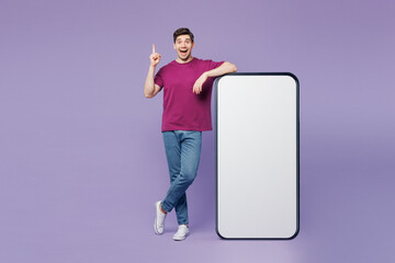 Poster - Full body young man in violet t-shirt casual clothes big huge blank screen mobile cell phone smartphone with workspace copy space mockup area hold finger up isolated on plain light purple background