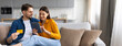 © Prostock-studio - A young couple sits comfortably on a sofa, exploring their tablet and discussing purchases. They seem engaged and happy, creating a warm atmosphere in their modern living space.