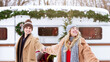 © Prostock-studio - A cheerful couple holds hands in a snowy landscape, laughing and enjoying their time together outside a cozy camper van decorated for the holidays. Festive greenery adds charm to the scene.