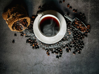 Wall Mural - Americano coffee cup and roasted coffee beans falling in a burlap sack on gray background, Black coffee cup aromatic,Top view