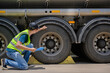© เลิศลักษณ์ ทิพชัย - A safety inspector inspects the tires of a big fuel tanker while wearing a reflective vest. He maintains adherence to transportation safety regulations while holding a clipboard.