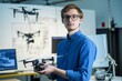 © Anzhela - Young European man in glasses operating drone in high tech lab surrounded by monitors and blueprints