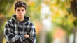© James - Serious teenage boy wearing plaid hoodie standing with crossed arms against blurred autumn foliage background, copy space