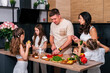 © dvulikaia - Large family - mom, dad and four daughters together prepare salad for lunch in modern kitchen. Big family together concept.