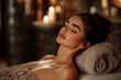 © bluecreamy - Woman relaxing in a spa, lying down with her eyes closed, covered with a towel, in a cozy and warmly lit environment with candles, a calm, serene, and soothing mood