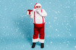 © deagreez - Full length photo of funny funky fat modern santa claus with big belly show index finger speechless sign hold gift box want give wish for eve wear red cap suspenders isolated blue color background
