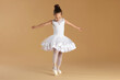 © New Africa - Little ballerina practicing dance moves on beige background