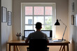 © MariiaDemchenko - Man working at desk with computer in home office, silhouette view, natural light, modern workspace