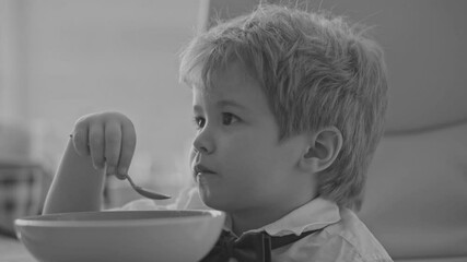 Wall Mural - Baby eats with a spoon. Child have a meal. Little kid eating kids food. Baby porridge. Little baby eating healthy food of dishes. A cute fun baby eating her dinner. Kids facial expression.