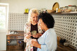 © Marko Geber - Mature lesbian couple laughing at smartphone in the kitchen with coffee