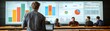 © ngstock - A person stands in front of large screens displaying colorful graphs and data, engaging an audience in a collaborative setting.