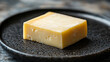 © SashaMagic - Close-up of a block of cheese on a dark plate.