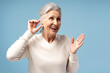 © Maria Vitkovska - Happy, attractive senior woman having hearing aid in ear, posing isolated on blue background