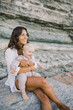 © Irina Efremova/Stocksy - Mother holding smiling baby while sitting on a rock at the beach