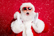 © deagreez - Closeup portrait photo of retired old man open mouth yelling palms mouth share information about newyear sales wear santa costume sunglass headwear isolated red color background