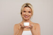 © Anastasiya - Best Cosmetics. Attractive Middle Aged Woman Holding Jar With Moisturising Cream And Smiling At Camera, Beautiful Mature Female Wrapped In Towel Showing Beauty Product For Anti-Aging, Copy Space. High