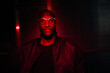 © Yakov Knyazev/Stocksy - Man illuminated by red light wearing glasses against dark striped back