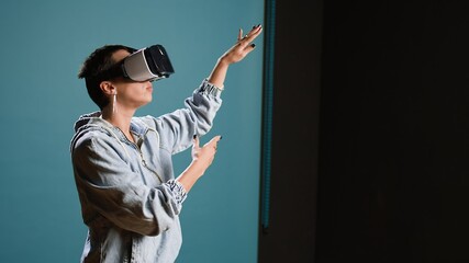 Wall Mural - Groovy edgy woman wearing a 3d virtual reality headset in studio, using artificial intelligence and glasses against blue background. Modern funky girl with style uses a modern gadget. Camera A.